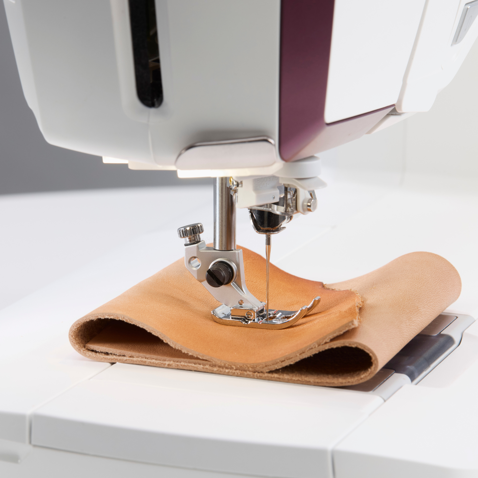 Sewing machine stitching a piece of leather on a white surface