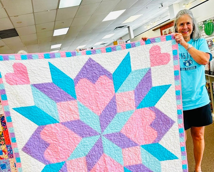 Woman holding a colorful quilt with heart patterns in a room.