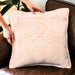 Beige pillow with floral pattern held by a hand on a brown couch