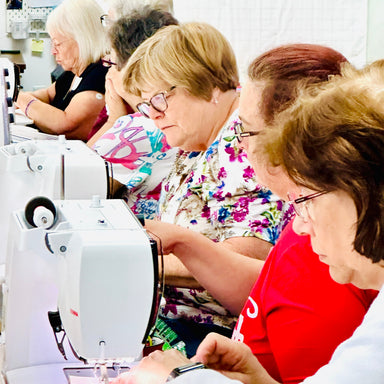 Group of people using sewing machines in a workshop setting.