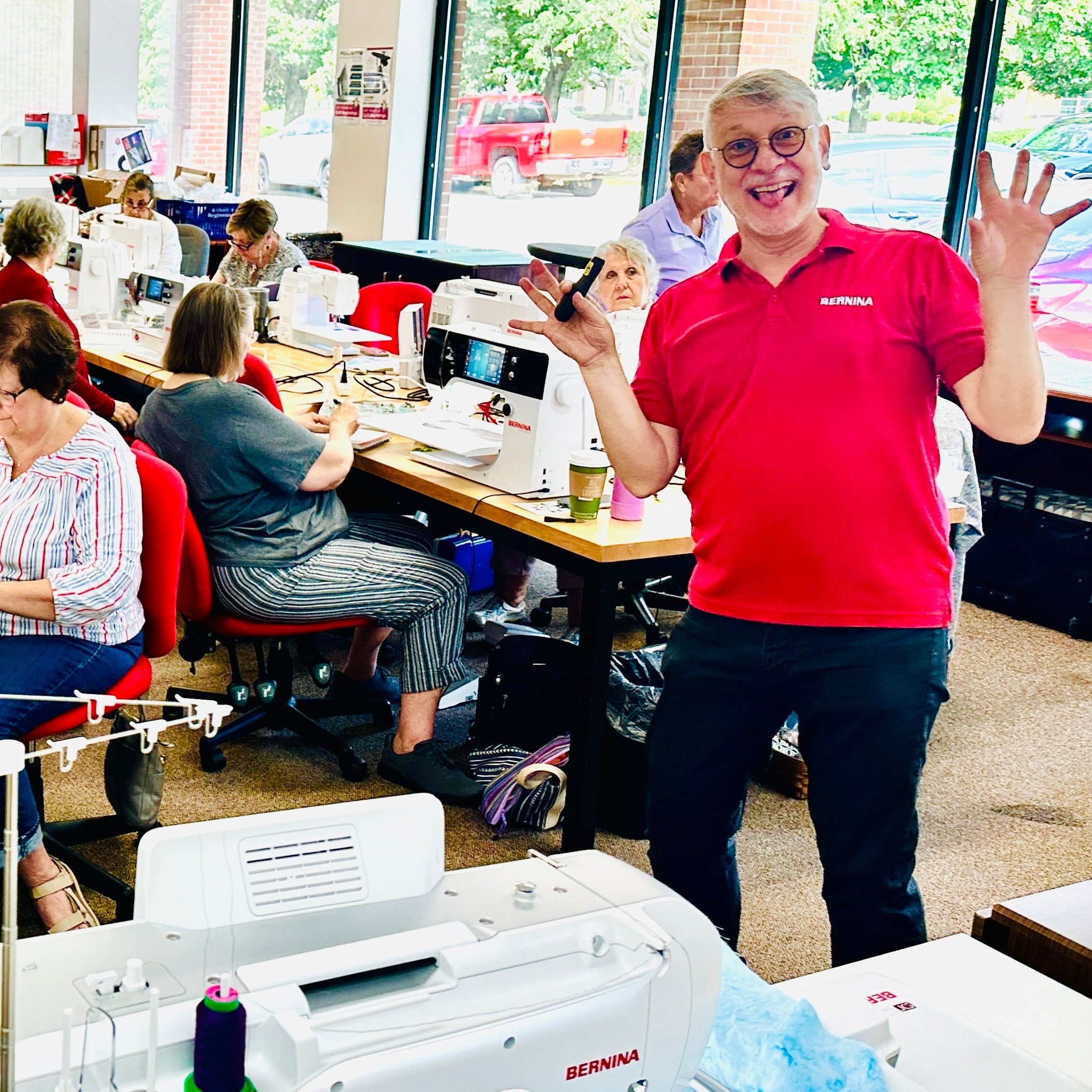 Person in a red shirt standing in a sewing room with multiple sewing machines and people working.