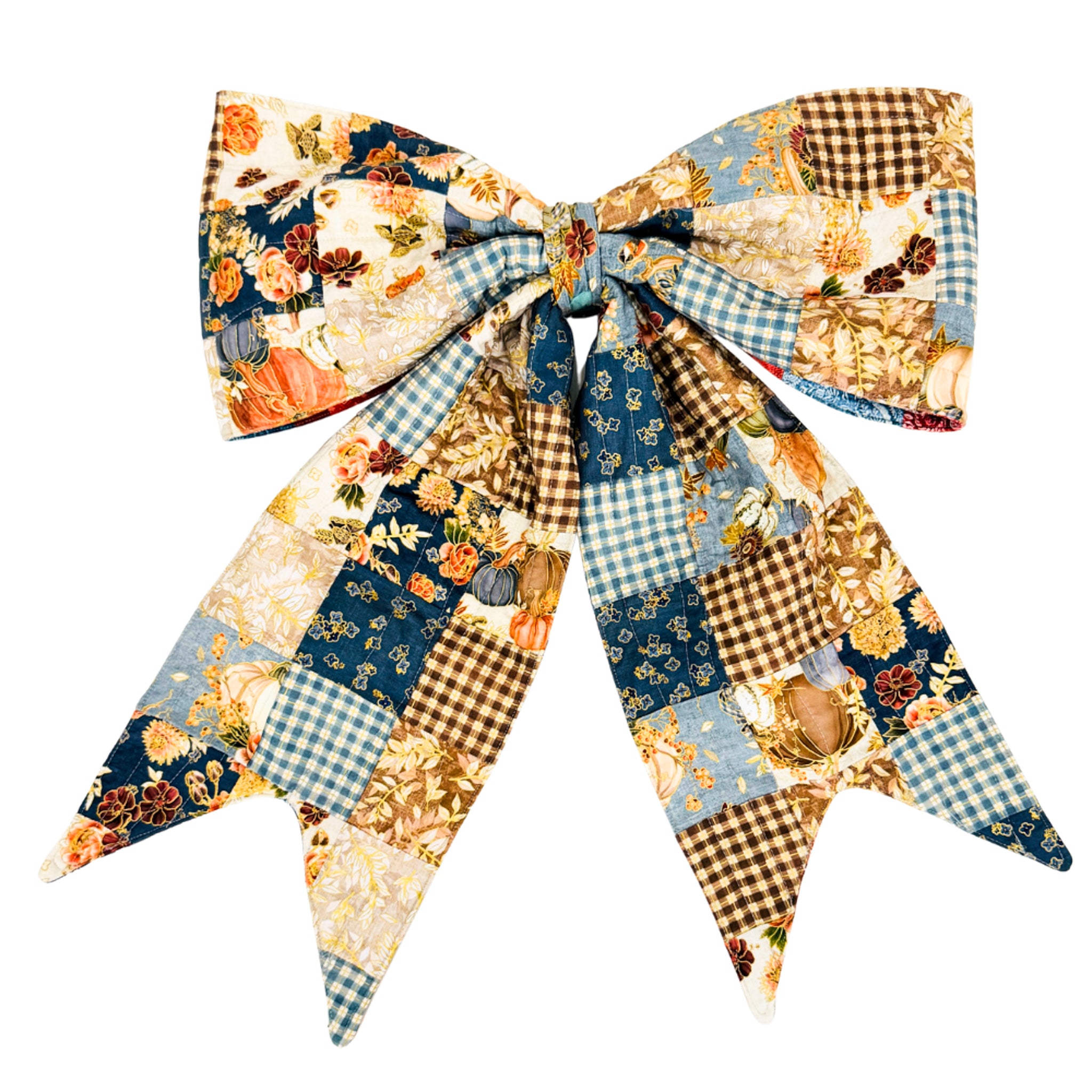 A large fabric bow featuring a patchwork design with gingham, floral, and pumpkin motifs in navy blue, beige, brown, and light blue, photographed on a solid white background.