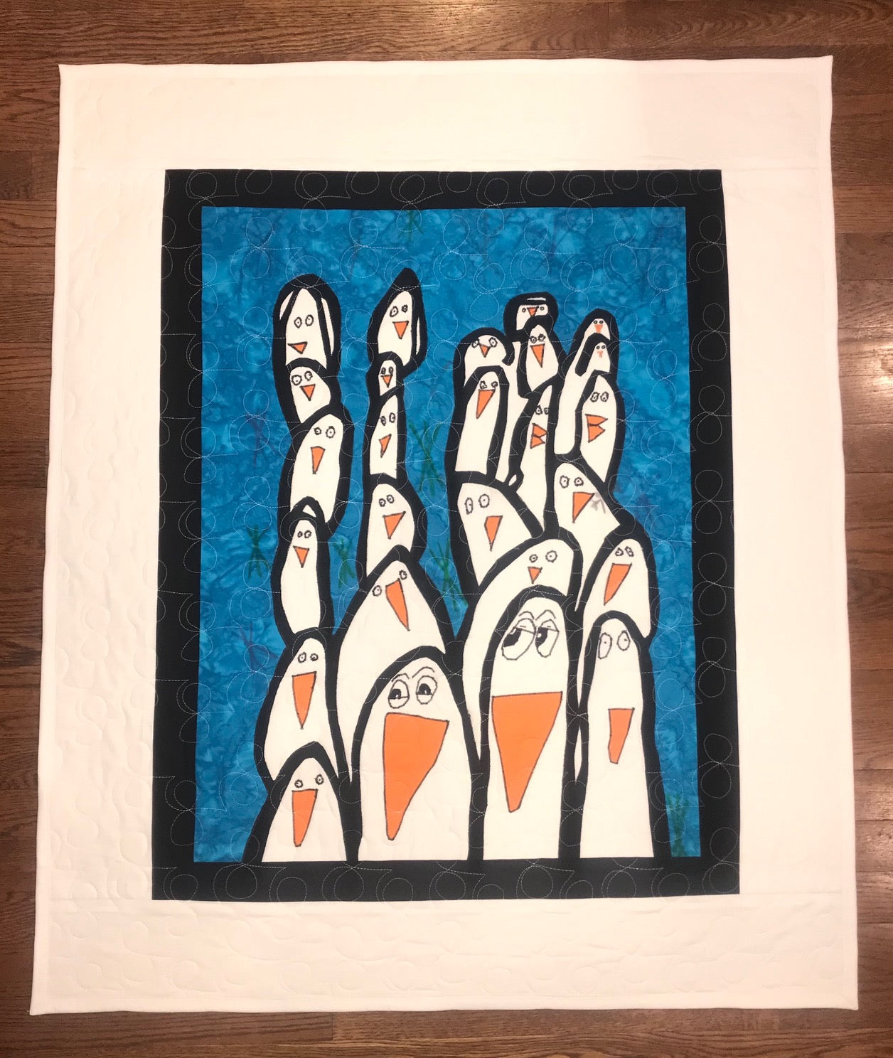 Quilt with penguin design on a blue background, displayed on a wooden surface.