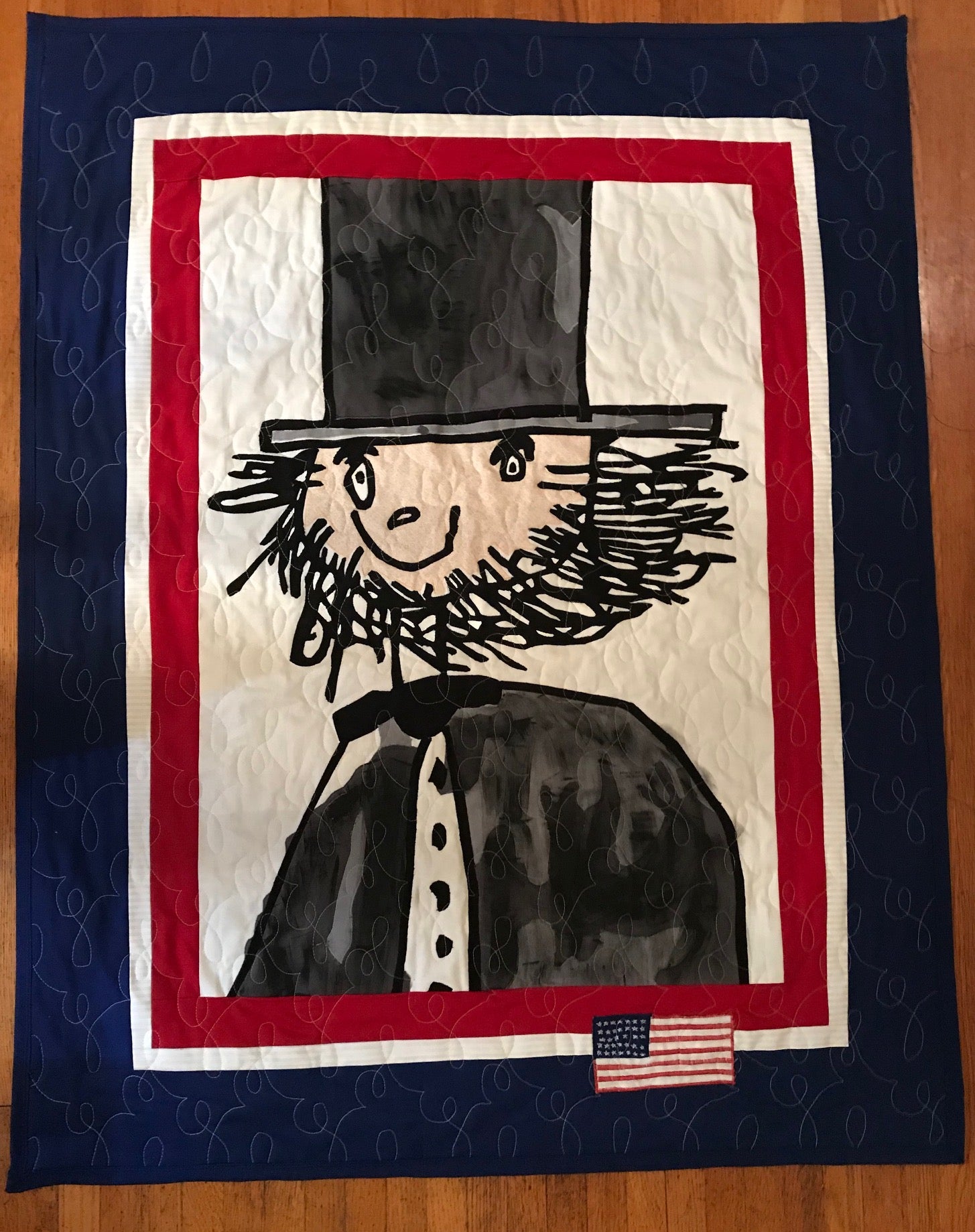 Quilt with a black and white illustration of a character wearing a top hat and bow tie, framed by a red, white, and blue border.