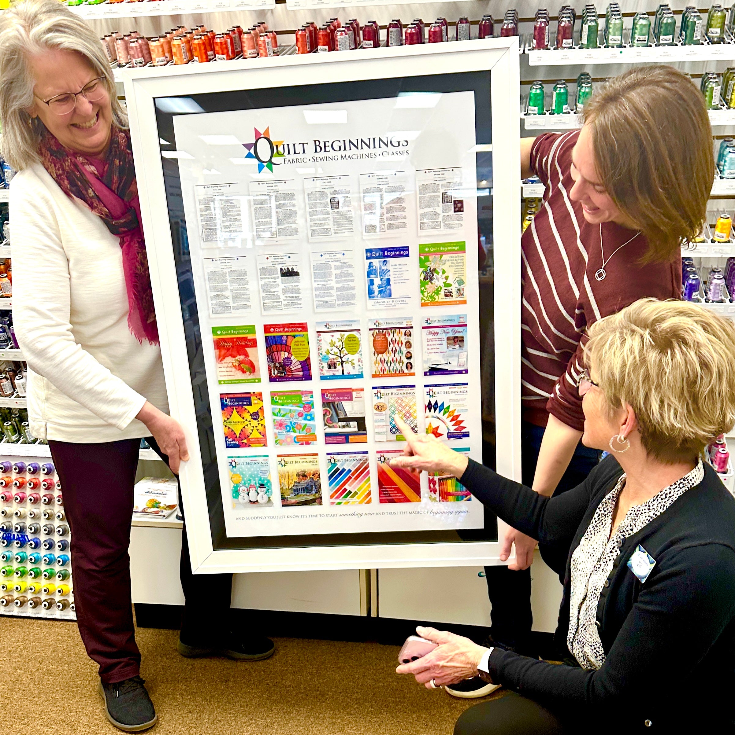 Three women looking at a framed poster in a store setting.