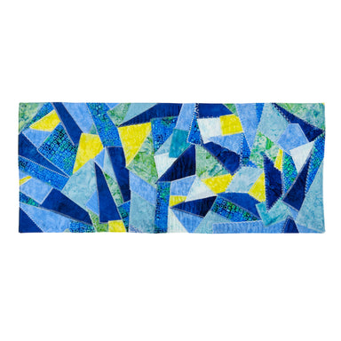 A rectangular patchwork quilt featuring an abstract geometric pattern of blue, navy, light blue, green, and yellow triangles, displayed flat against a solid white background.