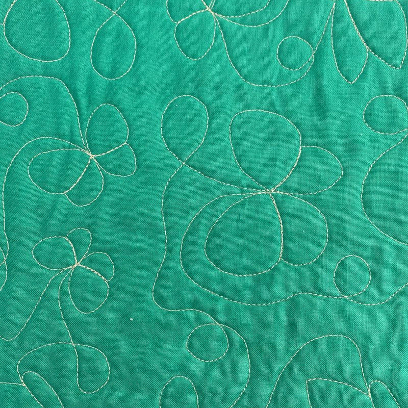 A close-up of a green quilted fabric featuring stitched floral and abstract leaf patterns in a contrasting light beige or cream thread.
