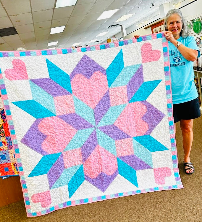 Woman holding a colorful quilt with heart patterns in a room.