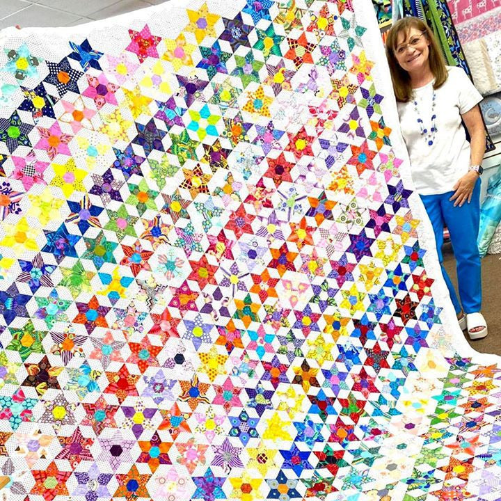 Colorful quilt with star patterns displayed on a table, with a person standing next to it.