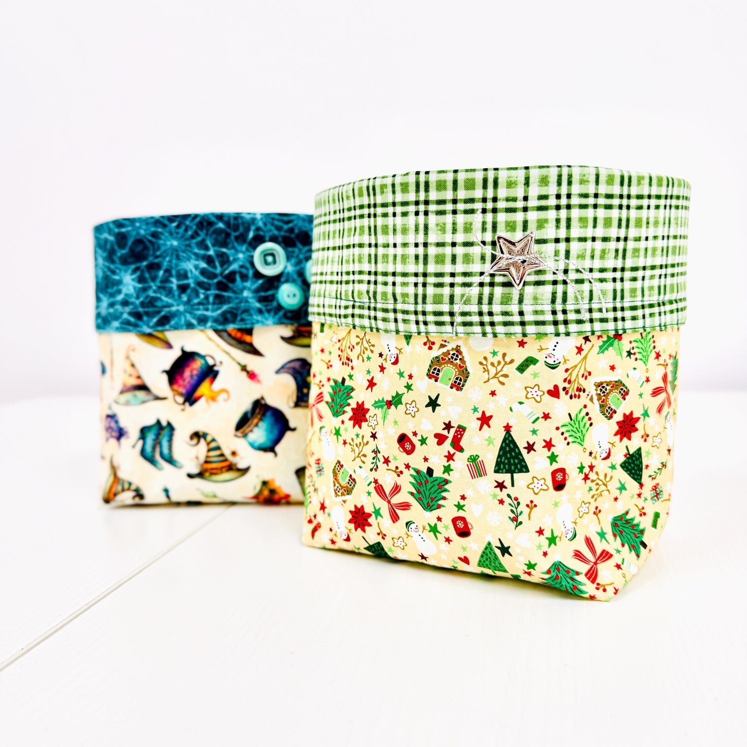 Two fabric storage boxes with buttoned flaps, shown on a white background. The box in front has a green plaid top band and a cream holiday print lower half.