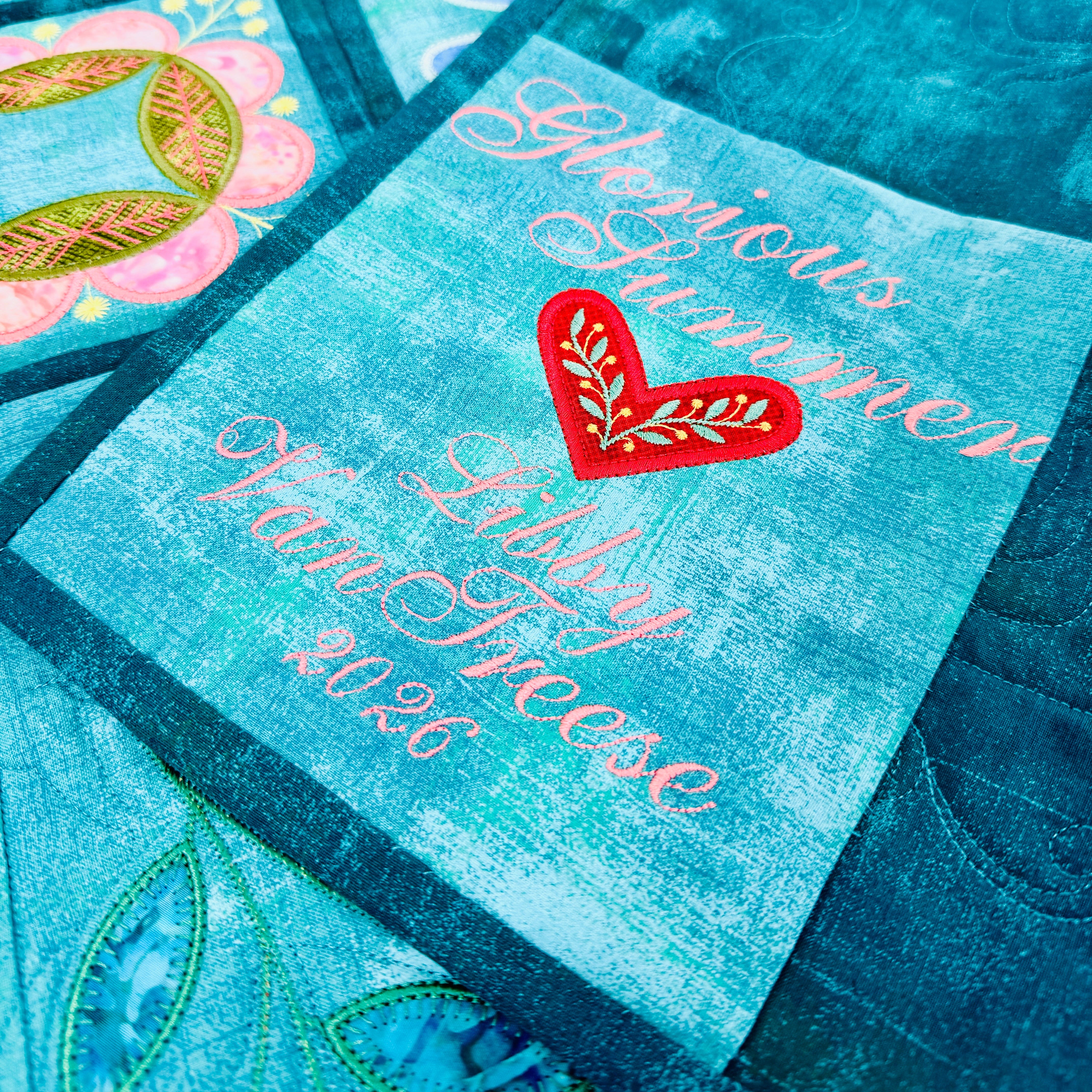 Close-up of a quilt with embroidered text and heart design on a blue background