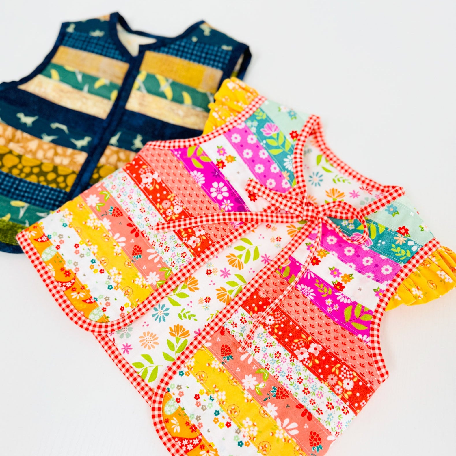 Two sleeveless patchwork vest-style tops laid flat on a white background. The front vest is bright multicolor with floral and striped panels in pink, orange, yellow, teal, and white, with red gingham trim.