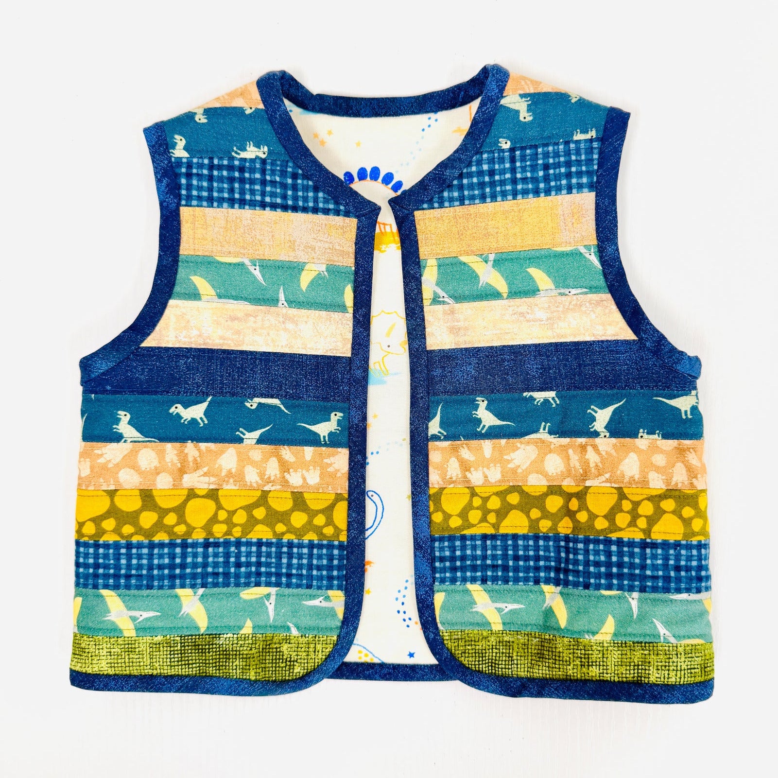A sleeveless quilted vest with horizontal striped panels in navy blue, teal, yellow, and beige, featuring various animal and bird patterns, laid flat on a white background.
