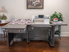 Sewing machine on a large gray table with a floral patterned fabric, in a room with a painting and plants.