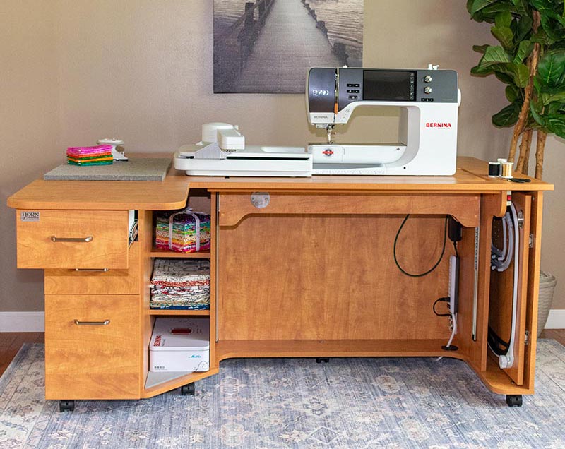 Wooden sewing desk with a Bernina sewing machine in a home setting.