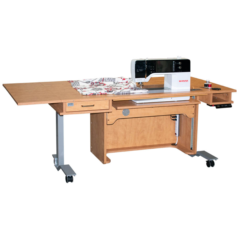 A white, height adjustable sewing table with an electric lift and a filler panel, equipped with wheels for mobility.