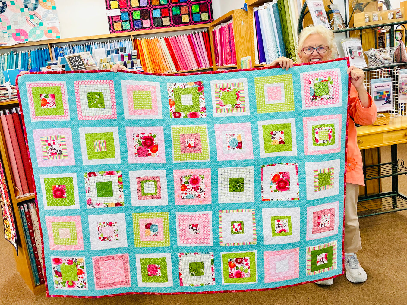 Person holding a colorful quilt with a pattern of squares in a room with bookshelves.