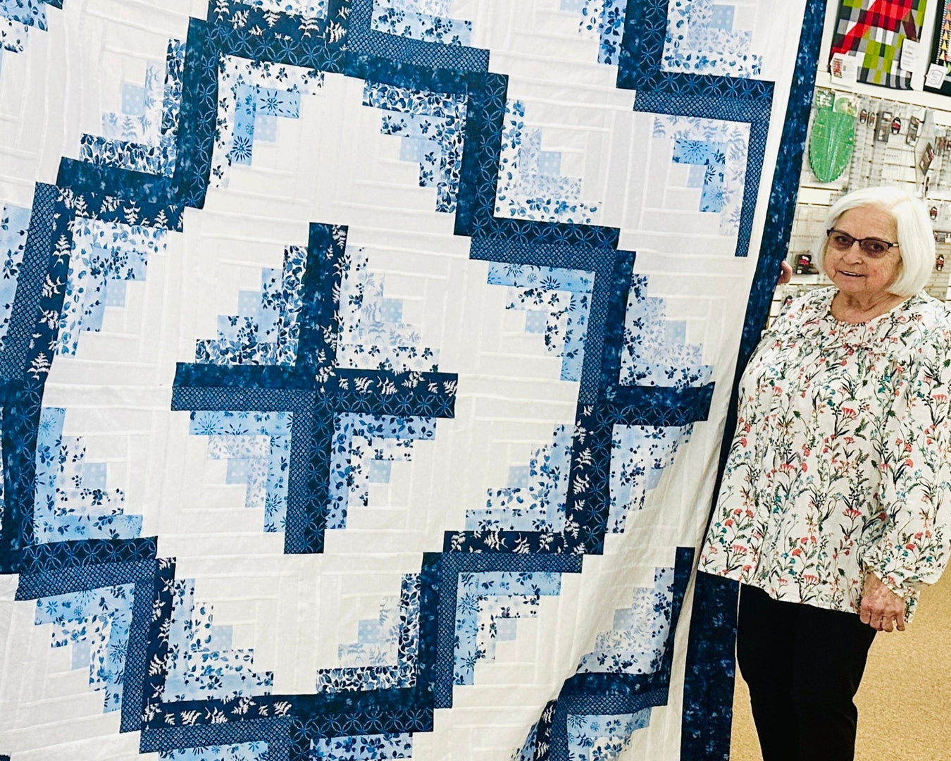Woman holding a large blue and white quilt in a store setting