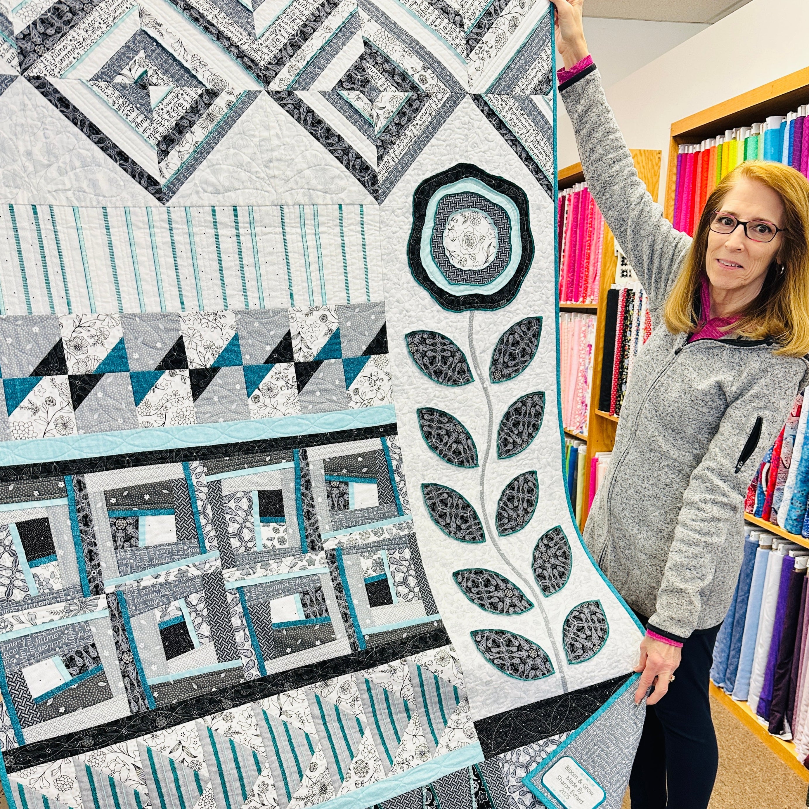 Woman holding a Bloom & Grow quilt with geometric patterns in a fabric store.