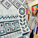 Woman holding a Bloom & Grow quilt with geometric patterns in a fabric store.