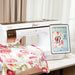 Sewing machine with a digital display and floral fabric on a table.