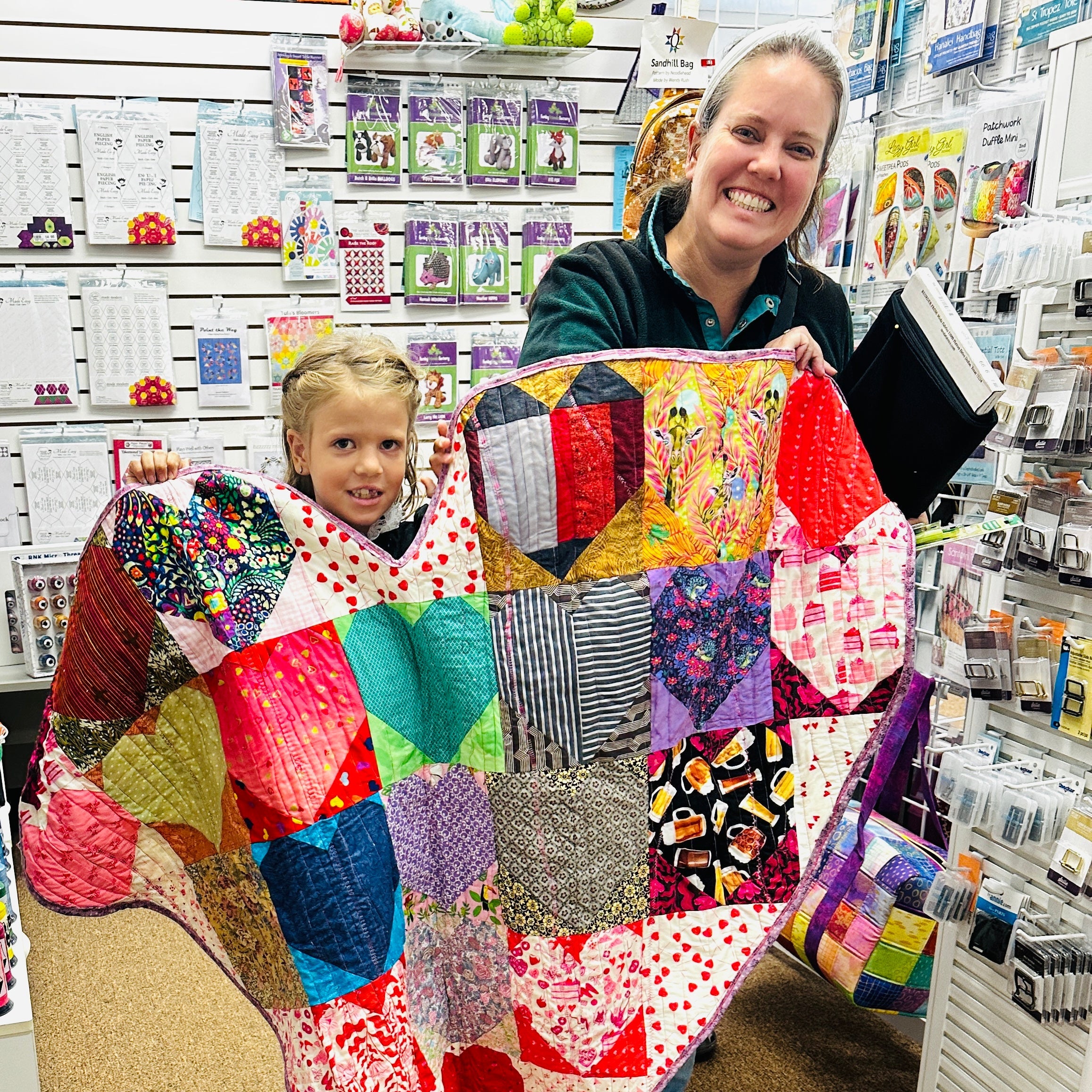 Two people holding a colorful patchwork quilt in a store setting.
