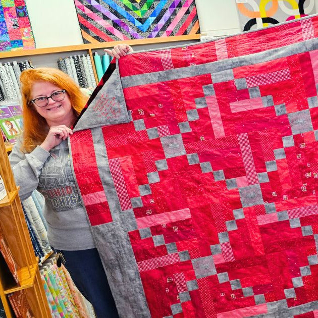 Person holding a red and gray quilt in a store setting