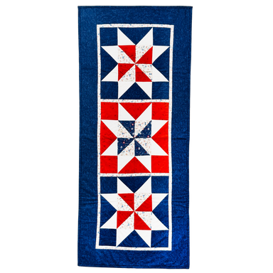 A vintage-style quilt runner featuring three vertical panels with red, white, and blue starburst patterns, finished with a wide blue border.