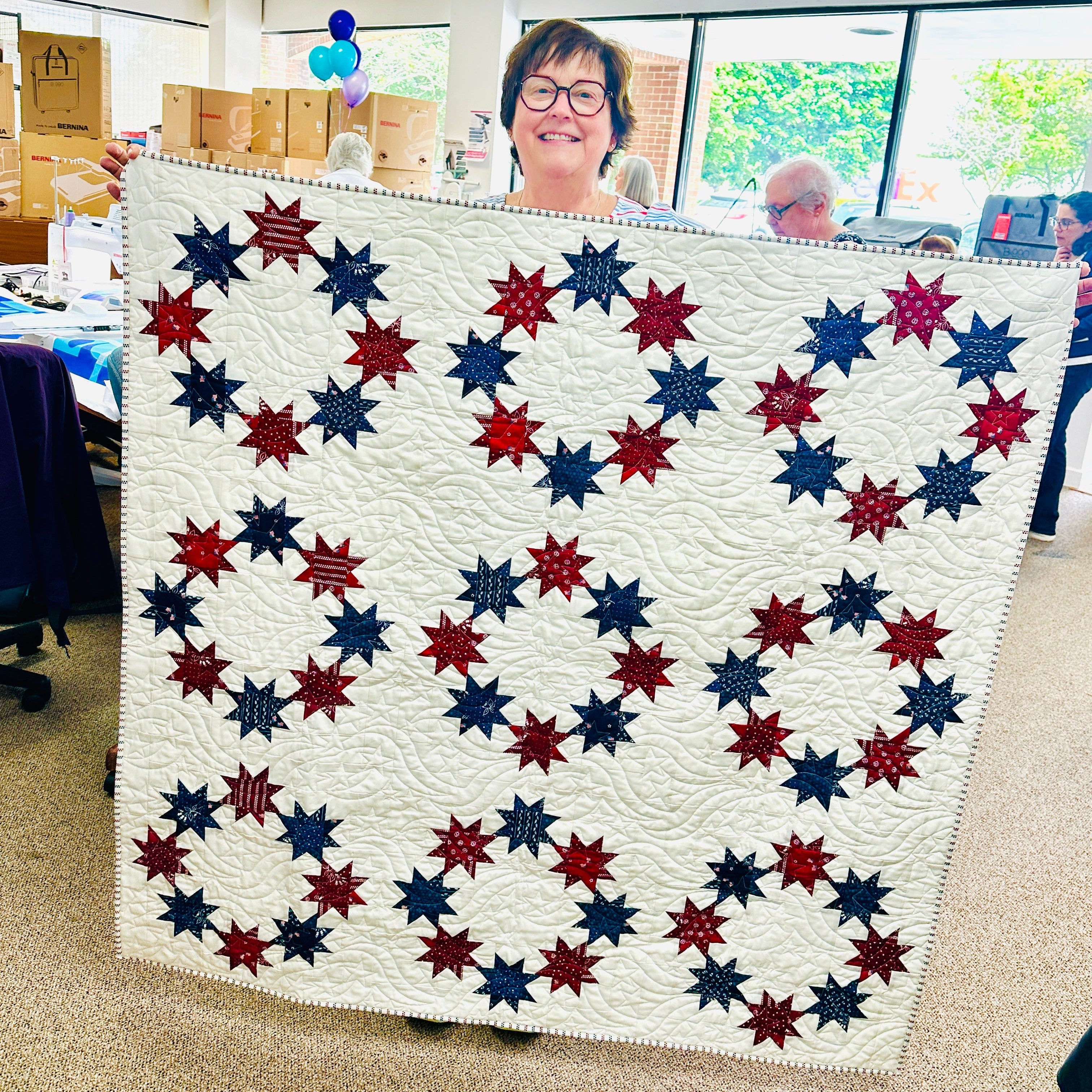 Person holding a large quilt with red, white, and blue star pattern in an indoor setting.