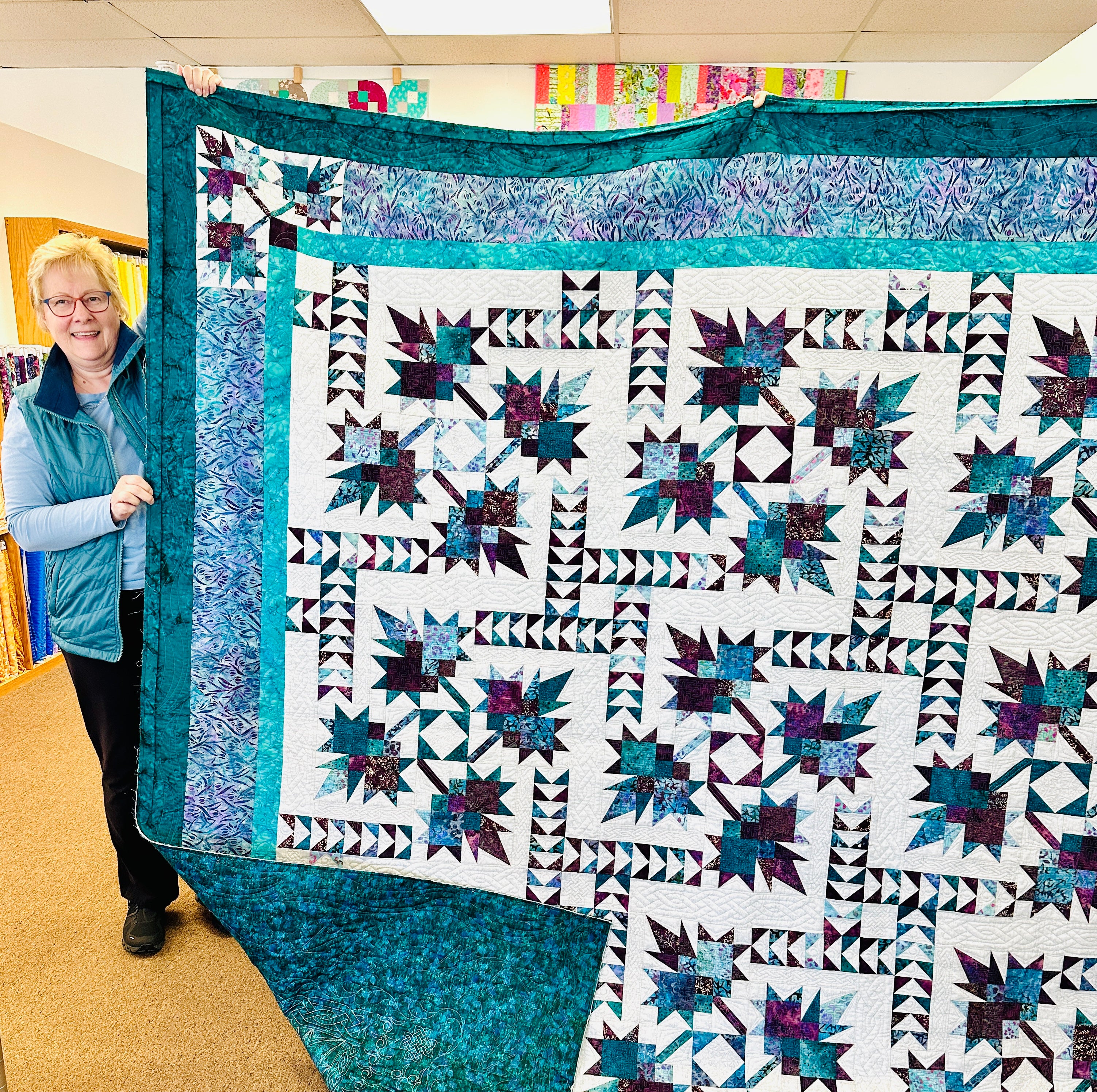 Person holding a large, colorful quilt with star patterns in a room.