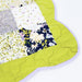 A close-up of a quilted patchwork blanket with a bright lime green border and floral patterned sections on a white background.