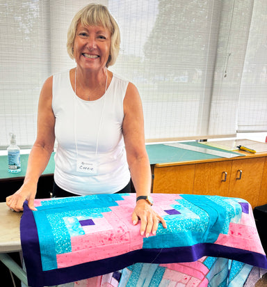 Woman standing behind a quilt in a room with tables and chairs.
