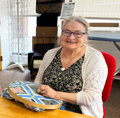 Woman sitting at a table with a decorative tray, smiling in an indoor setting.