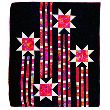 A square quilted textile featuring a black background with four starburst motifs in white and bright pink, red, orange, and purple patterned fabric, connected by vertical striped columns in pink, white, and black.