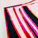 A close-up of a handmade quilted fabric piece with alternating wide light pink panels and narrow black panels trimmed in bright multicolor floral ribbon, photographed on a white background.
