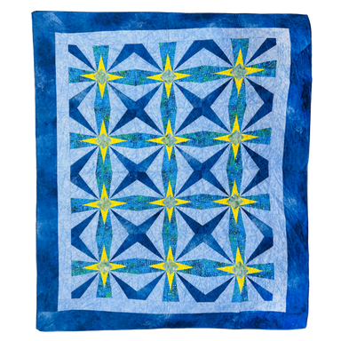 A square quilt with a geometric starburst pattern, featuring shades of blue, navy, and yellow on a white background with a blue border.