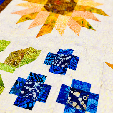 Quilt block with sunflower design featuring blue leaves on a white background