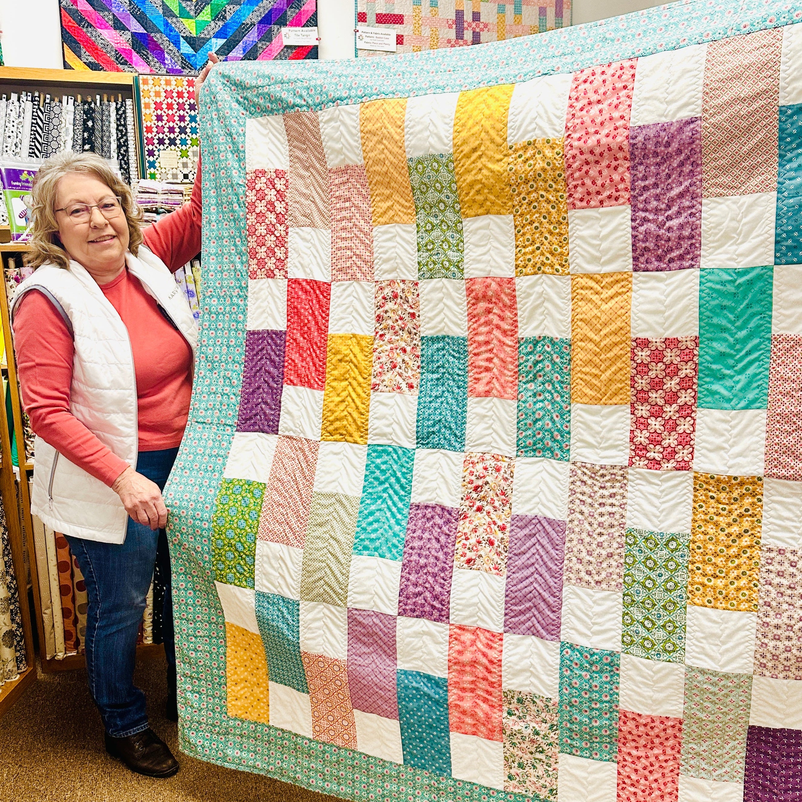 Woman holding a colorful patchwork quilt in a fabric store.
