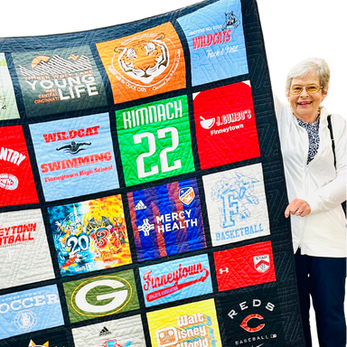Quilt made from various t-shirts with different designs and text, held by a person.