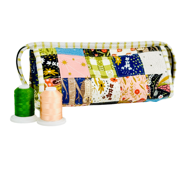 Patchwork-patterned fabric roll with spools of thread on a white background
